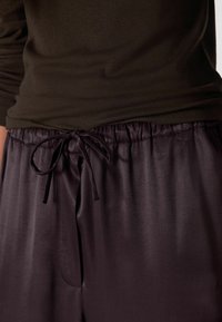 Ciemnofioletowe satynowe spodnie od piżamy z talią na sznurek, gładką fakturą i bocznymi kieszeniami; w zestawieniu z dopasowanym oliwkowozielonym prążkowanym topem.