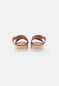 Tan leather sandals with ankle straps, woven jute midsole, and white rubber sole. Smooth texture, open-back design, and simple buckle detail.
