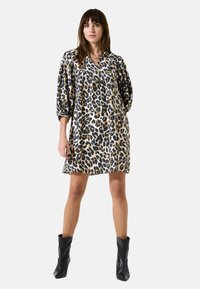 Vestido de estampado de leopardo en una tela suave, con un corte holgado, mangas tres cuartos y escote en V. Combinado con botas negras hasta la rodilla.