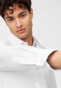 Witte button-up shirt met lange mouwen, voorzien van een klassieke kraag en parelknopen. Gladde stoftextuur en een getailleerde pasvorm.