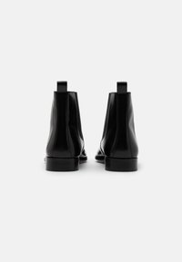 Černé kožené kotníkové boty s hladkým povrchem, zaoblenou špičkou, táhly na obou stranách a elastickými postranními panely pro elegantní vzhled.