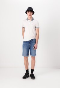 Hvit polo-shirt med mørke detaljer, denimshorts, svart bøttehatt, svarte sneakers og svarte sokker. Uformell antrekk vist.