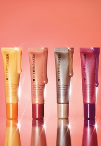 Cztery tubki wyciskane z balsamem do ust w odcieniach złotym, brzoskwiniowym, beżowym i różowym, z błyszczącymi akcentami i refleksyjnymi powierzchniami na gradientowym tle.