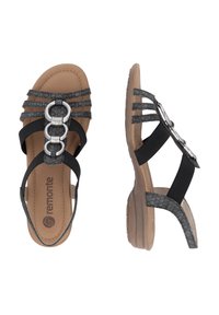 Schwarze und graue Sandalen mit elastischen Riemen, einer gepolsterten, tanfarbenen Innensohle und einem silbernen, runden Hardwareakzent auf der Vorderseite. Niedriger, texturierter Absatz.