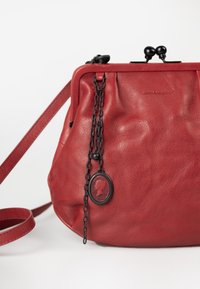 Rote Lederhandtasche mit strukturierter Oberfläche, plissiertem Design, schwarzem Kettenakzent und einem runden Anhänger mit einer Profil-Silhouette.