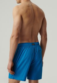 Niebieskie szorty kąpielowe z teksturowanej tkaniny, elastycznym paskiem w talii i małą kieszonką z tyłu. Projekt jest prosty i funkcjonalny.