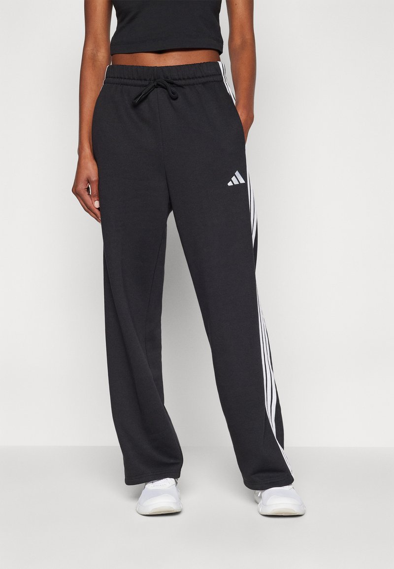 Juodos sportinės kelnės su laisvu sijonu, su baltais trimis dryžiais šonuose, elastinga liemene su raišteliu ir „Adidas“ logotipu ant šlaunies.