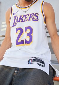 Weißes Basketball-Trikot mit lila und gelben Akzenten, ausgestattet mit "LAKERS" und der Nummer "23". Nike-Logo und NBA-Tag am Saum. Netzstruktur.