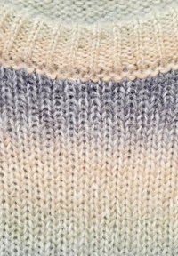 Pletena tkanina z gradacijskim prehodom barv od kreme do sive. Teksturirana, mehka volnena preja z vidnimi šivi in subtilnim sijajem.