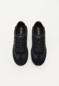 Sorte sneakers laget av semsket skinn og syntetisk materiale, med snøring, hvit såle og gull detaljer på hælen og logoen.
