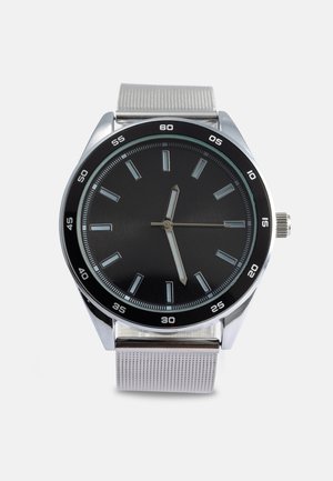 Runde Uhr mit schwarzem Zifferblatt, silbernen Stundenmarkierungen und silbernem Milanaise-Armband. Verfügt über ein silbernes Gehäuse und eine schwarze Lünette mit Minutenmarkierungen.