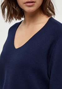Maglione a coste blu navy con scollatura a V profonda, caratterizzato da una texture morbida e una vestibilità rilassata, che evidenzia la semplicità e la versatilità del capo.