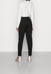 Černé kalhoty na míru s elastickým pasem, v kombinaci s bílým texturovaným topem. Modelka má na sobě béžové sandály na blokovém podpatku.