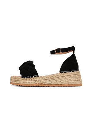Schwarze Espadrille aus Wildleder mit einer Sohle aus gewebtem Jute, ausgestattet mit einem geflochtenen Knotendetail vorne und einem verstellbaren Knöchelriemen.