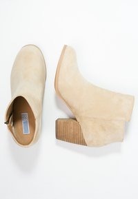 Beige suède enkellaarsjes met een ribbelige bruine blokhak. Voorzien van een zijrits voor sluiting en een afgeronde neusontwerp.