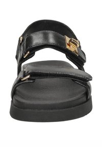 Zwarte slip-on sandaal met brede banden, gouden gesp detail, platte zool en een gladde textuur, die een minimalistisch en hedendaags ontwerp benadrukt.