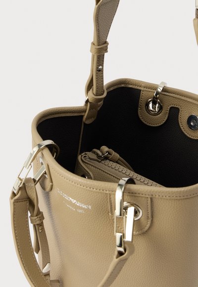 Μπεζ δερμάτινη τσάντα τύπου bucket με ασημί μεταλλικά στοιχεία, με υφή και μαύρο εσωτερικό. Περιλαμβάνει μια μικρότερη τσέπη με φερμουάρ στο εσωτερικό.