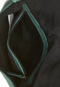 Svart tygväska med inredning i grönt mocka längs toppen. Innehåller en zip-försedd fack med svart dragkedja och tygfoder.