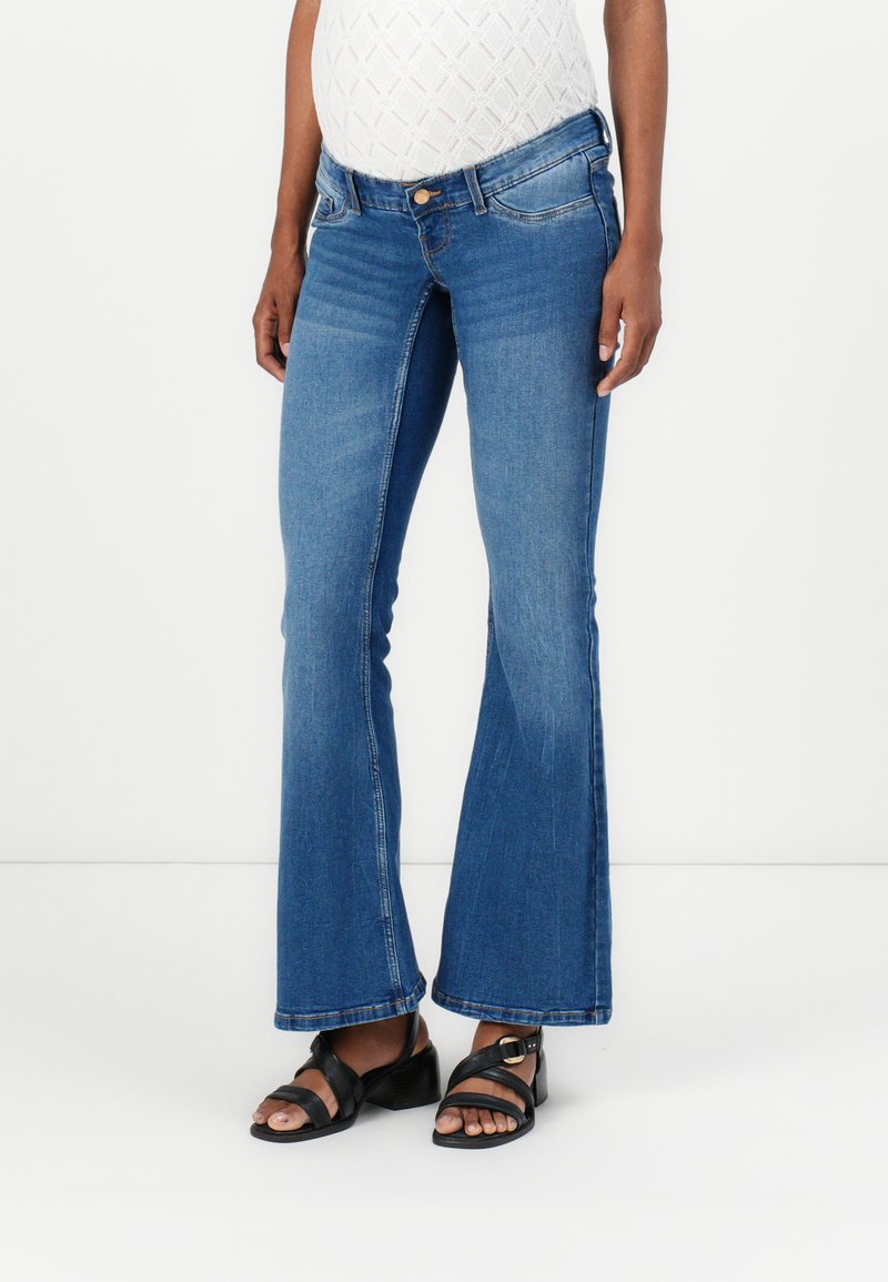Blå flared jeans med middels høy midje, detaljert søm og frontlommer. Kombinert med svarte sandaler med stropper som viser en blokkhæler.