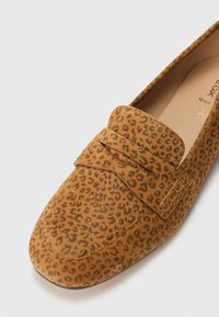 Mocassins en suede beige à motif léopard, avec une semelle plate et une sangle décorative sur le devant. Texture lisse.