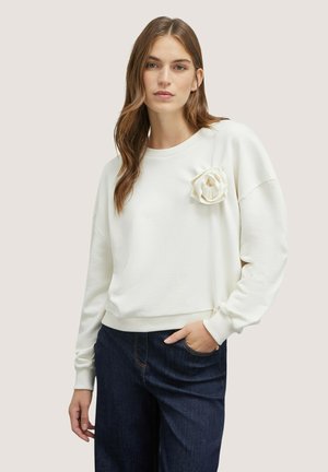 Witte sweatshirt met een gestructureerde afwerking en een 3D roos detail op de borst, gecombineerd met donkerblauwe wijde denim broek.