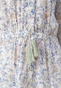 Tissu léger avec imprimé floral et cachemire en bleu, rose et olive, devant boutonné et taille nouée avec deux pompons vert clair.