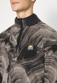 Fleece pullover met een half-zip ontwerp, met een zwart en grijs gemarmerd patroon en een klein logo op de borst. Soepele textuur.