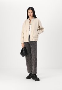 Veste bomber en polaire beige avec boutons-pression et deux poches avant, associée à un jean noir à motif étoile et des bottes noires à lacets.