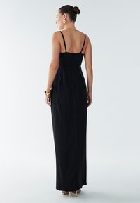 Black satin maxi dress with thin straps, fitted bodice, and a flowy silhouette. Back zipper detail and minimal design for a classic look.