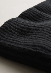 Crna pletena tkanina s istaknutim rebrastim uzorkom. Mekana i topla, materijal se nježno preklapa, prikazujući valovite nabore.