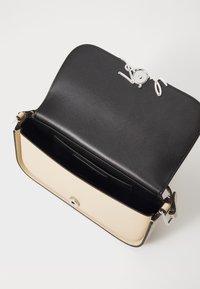 Borsa in pelle nera e crema con una texture liscia, accessori in argento e un design a patta aperta che mette in mostra un interno spazioso.