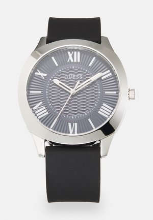Orologio con cinturino in silicone nero e cassa in tono argento, quadrante grigio testurizzato con numeri romani e lancette argento. Nome del marchio "GUESS" in evidenza.