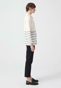 Lekki sweter dzianinowy w odcieniu kremowym, z szarymi poziomymi paskami, z kołnierzykiem. Zestawiony z czarnymi spodniami typu straight leg i loafersami.