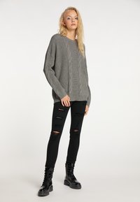 Grauer Kabelstrick-Pullover mit langen Ärmeln, kombiniert mit schwarzen, zerrissenen Skinny-Jeans und schwarzen Schnürstiefeln mit einer dicken Sohle.