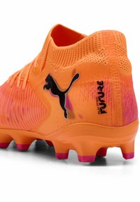 Scarpe da calcio arancioni brillanti con accenti viola, tomaia sintetica texturizzata e logo Puma nero; suola multi-terreno per terreni vari.