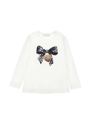 Chemise blanche à manches longues avec un nœud à pois noir et blanc et un pendentif cœur clouté doré imprimé sur le devant.