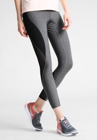 Leggings sportivi grigi a vita alta con pannelli in rete nera e cuciture eleganti, abbinati a scarpe da corsa grigie e rosa.