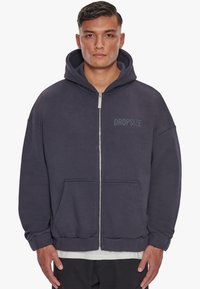Grå zip-up hættebluse med en stor kængurulomme, ribbede manchetter og snoretræk i hætten. Har "DROPSIZE" trykt på brystet.