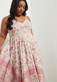 Vestido de estampado floral con escote en v, tirantes finos y detalles de pliegues. Tejido ligero en colores rosa y crema, con un dobladillo texturizado.