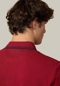 Červené polokošele s textúrovaným povrchom, s námořnícky pruhovaným golierom a vyšívaným nápisom "HACKETT" na zadnej strane krku.