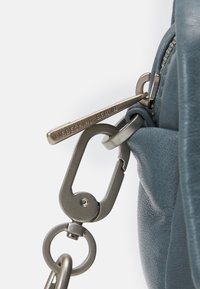 Borsa in pelle blu con una zip metallica argentata dotata di un tirante inciso con "LIEBESKIND BERLIN", collegato a un moschettone metallico e anello.