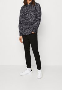 Mustapaitainen pitkähihainen paita, jossa on valkoinen lehvämalli, yhdistettynä mustiin slim-fit-housuihin ja valkoisiin tennaioihin, joissa on mustia yksityiskohtia.