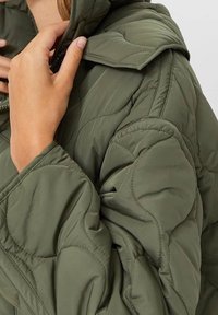 Olivgrüne Steppdaunenjacke mit gestepptem Design, hohem Kragen und Reißverschluss. Der Stoff wirkt glatt mit leicht glänzendem Finish.