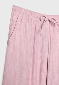 Pantalon en tissu texturé rose clair avec taille élastique et cordon de serrage. Comprend des poches latérales et un design à coupe décontractée.