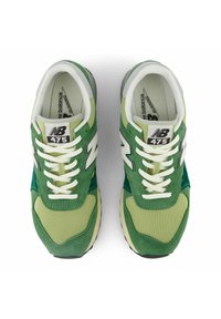 Sneakers verdi e verde chiaro in materiali scamosciati e mesh, con lacci bianchi, accenti argentati e un logo 'NB' ben visibile.