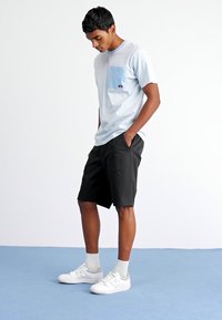 Lys blå stripete t-skjorte med en blå lomme, kombinert med svarte shorts og hvite sneakers. Glatt stoff og avslappet passform.