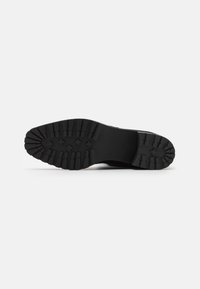 Suela de zapato negra con un patrón de textura, que presenta grips elevados y una puntera redondeada. Fabricada en goma para mayor durabilidad y tracción.