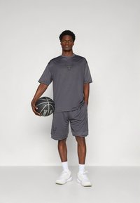 Pilkos spalvos sportinės šortai ir trumpomis rankovėmis marškinėliai iš lengvos medžiagos, su subtiliu logotipu, derinami su baltais sportbačiais ir krepšinio kamuoliu.