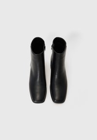 Botas de cuero negras hasta el tobillo con un diseño de punta cuadrada, textura suave y cierre lateral con cremallera. Silueta simple y elegante.