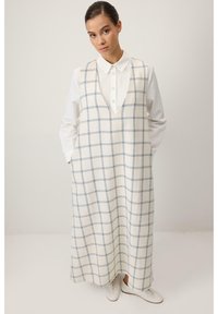 Robe longue sans manches en tissu crème avec un motif quadrillé bleu, dotée d'un décolleté en V profond, de poches latérales et d'une coupe ample.